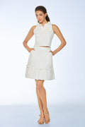 Woman wearing a white outfit with a top and skirt with hand-crafted floral details on a light blue background from vandamod designer woman fashion